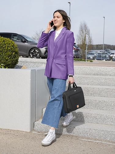 A young woman walks down a flight of steps outside, talking on the phone and casually carrying the Hama ‘Extreme Protect’ laptop bag in her hand.